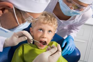 Image of dental examining being given to little boy by dentist and his assistant